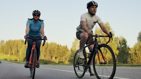 Steadicam-shot-of-two-healthy-mem-and-woman-peddling-fast-with-cycling-road-bicycle-at-sunset